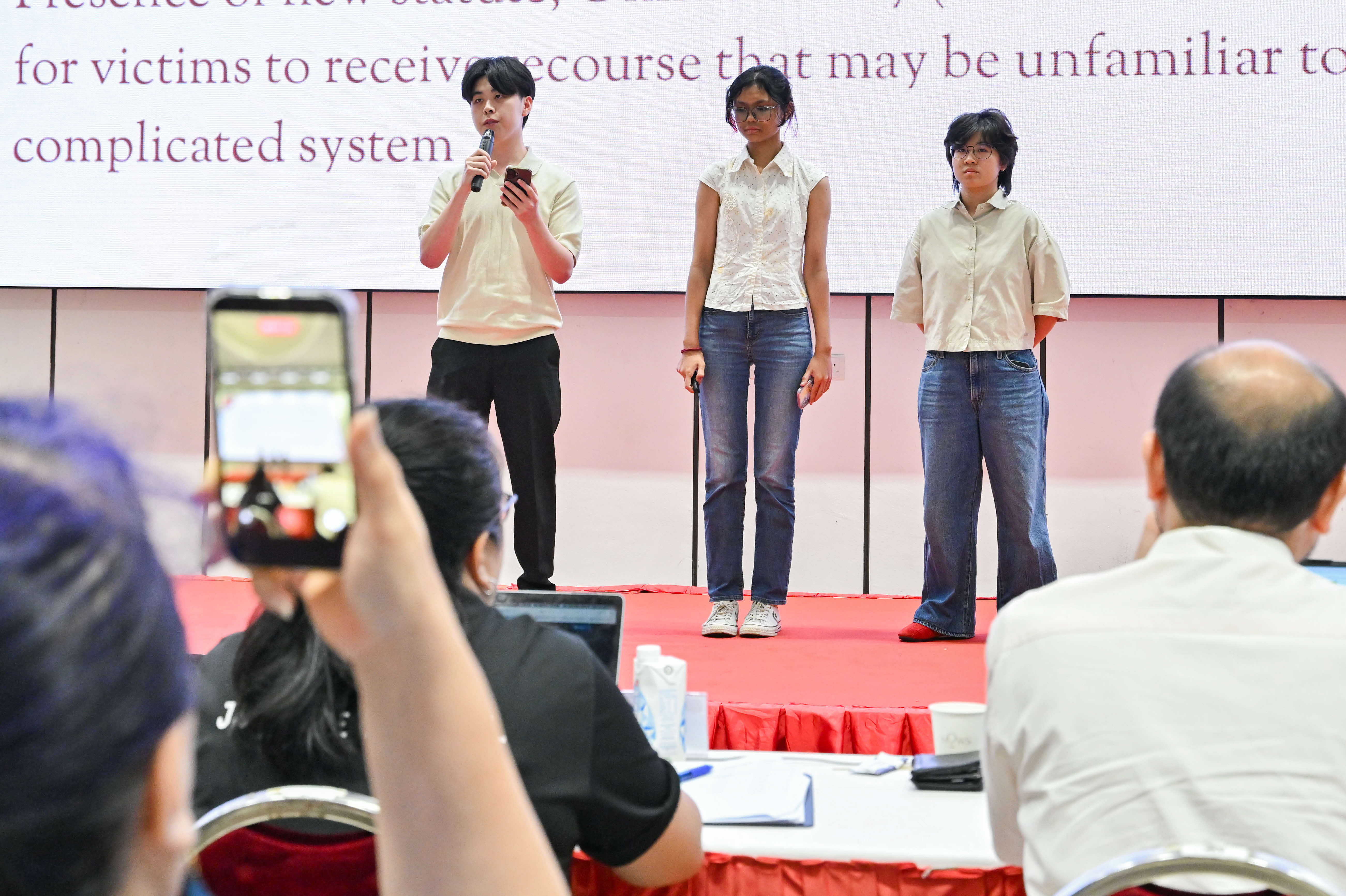 Audience member taking a video of three students presenting